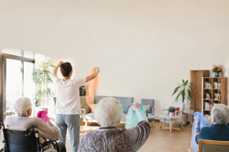Une animatrice guide un atelier de danse avec foulards colorés auprès de personnes âgées en EHPAD.